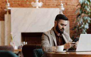 Man sitting at a table with a laptop using a phone to order food while working remotely