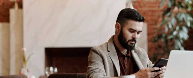 Man sitting at a table with a laptop using a phone to order food while working remotely