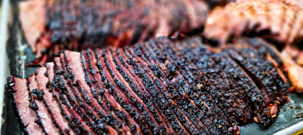 A large dark piece of crusted beef brisket on a wooden ZZQ platter.