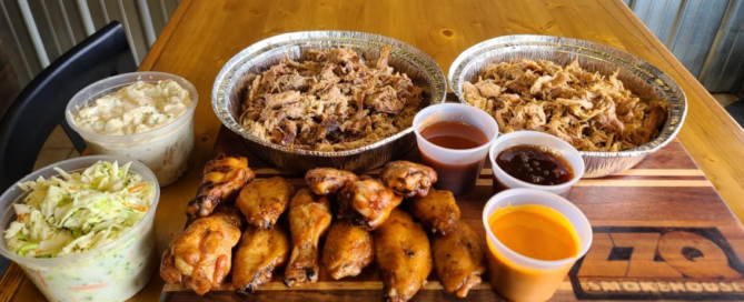 A delicious catering spread with trays of pulled meat, chicken wings, and various side dishes for an event.